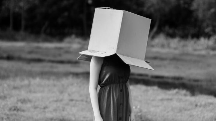 faceless woman with cardboard box on head against pond